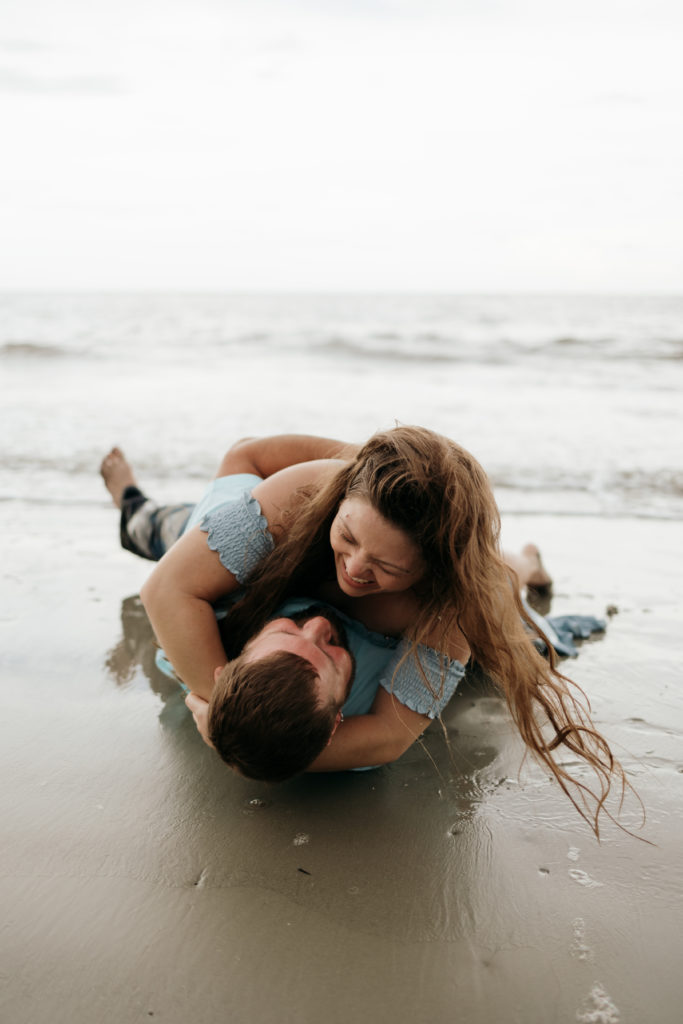 Newly engaged couple rolling in the sand at Jekyll Island Driftwood Beach engagement session