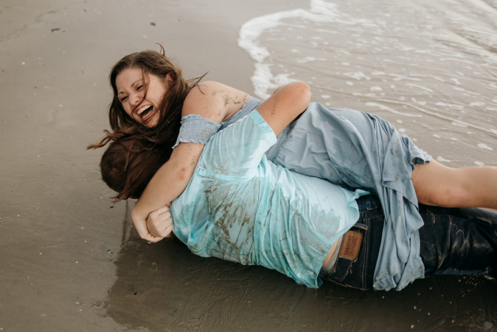 Newly engaged couple rolling in the sand at Jekyll Island Driftwood Beach engagement session