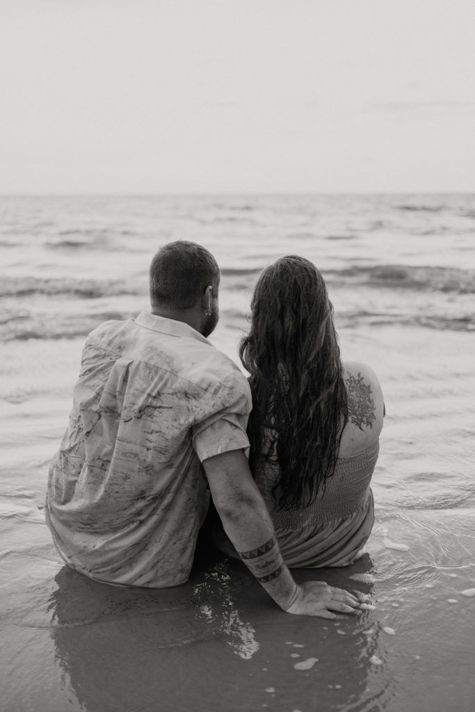 Newly engaged couple sitting on the beach at Jekyll Island Driftwood Beach engagement session