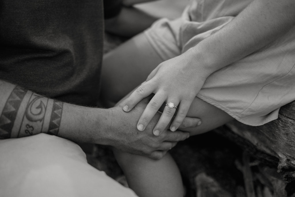 Couple holding hands with engagement ring at driftwood beach engagement session